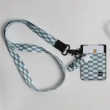 Llavero de cuello con cinta de tela estampada en tonos celeste y blanco, con detalles de cuero sintético negro y gancho mosquetón metálico.