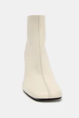 Botín de cuero color crema con puntera cuadrada y cierre de cremallera en la parte trasera. El tacón es ancho y de color negro. La altura del tacón es de 8,5 cm.