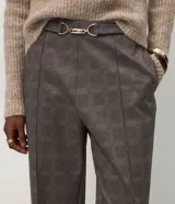 Pantalón de corte recto y entallado con estampado de cuadros escoceses. Presenta cintura estructurada con un aplique metálico decorativo en el centro y costuras verticales frontales que estilizan la silueta.