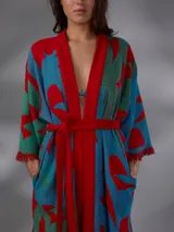 Kimono largo de algodón texturado con estampado vegetal en tonos rojo, azul y verde. Cuenta con mangas amplias, cinto independiente para ajustar a la cintura, bolsillos laterales y aberturas laterales en el dobladillo con detalles de flecos.