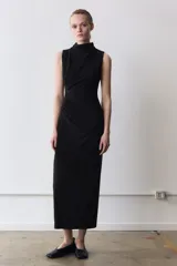 Vestido midi de color negro, con cuello subido y diseño sin mangas. Presenta un detalle de drapeado lateral en la parte delantera y cierre de cremallera oculta en la espalda.