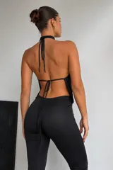 Catsuit negro de una sola pieza, con escote profundo tipo halter y espalda descubierta. Confeccionado en tela satinada con corte ajustado en el torso y piernas acampanadas.