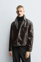 Cazadora cropped de hombre confeccionada en tejido efecto piel de acabado brillante y color marrón. Cuenta con cuello de solapas de muesca, manga larga con puños abotonados, bolsillos de vivo en la cadera y cierre frontal con botonadura.