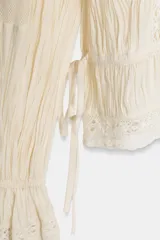 Blusa color crema de algodón con cuello alto, manga larga y bordados florales.