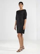 Vestido corto de punto con hilos metálicos que aportan un brillo sutil. Presenta un calce relajado, cuello redondo, mangas cortas y espalda en V pronunciada con detalle de dije metálico.