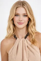 Mono largo de color nude, con escote halter y detalle de cadena en el cuello. Presenta una silueta relajada con pantalón de corte recto y fluido.