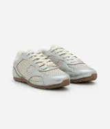 Championes de estilo urbano inspirados en botines de fútbol, confeccionados en poliuretano plateado con paneles de malla transpirable. Presentan cierre con cordones, punta redondeada y suela plana de goma en color marrón.