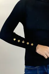 Polera de hilo blanca de cuello alto y manga larga, con detalle de botones dorados en los puños. Tejido de punto acanalado ajustado al cuerpo.