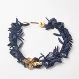 Collar de diseño orgánico compuesto por múltiples piezas pequeñas de resina en color azul oscuro, con un aplique central de piezas metálicas doradas y cierre de botón.