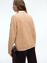Cardigan de punto color beige con cierre frontal de botones, cuello en V y dos bolsillos delanteros. Presenta mangas largas con puños acanalados y un diseño de corte holgado.