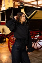 Camisa de lino color negro con cuello alto, volados frontales y mangas largas abullonadas con puños elásticos. Presenta cierre frontal con botones ocultos.