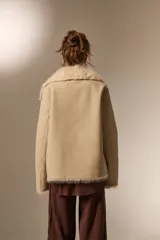 Chaqueta de eco-cuero color beige con interior y cuello de piel sintética al tono. Presenta un diseño holgado, cierre frontal con un botón y solapas amplias.