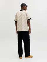 Camiseta tipo polo de manga corta con calce suelto. Presenta un diseño de cuadros en tonos beige y crema, con cuello y bordes de mangas en color negro. Incluye un escudo circular bordado en el pecho y estampado tipográfico en el frente.