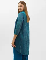 Conjunto de tres piezas compuesto por musculosa, cardigan y pantalón. La musculosa y el cardigan presentan un diseño plisado con hilos metalizados en tonos verdes y azules, creando un efecto tornasolado. El cardigan es de frente abierto con mangas 3/4 y corte fluido. El pantalón es de seda fría en color azul petróleo, con cintura elastizada. Incluye un collar removible.