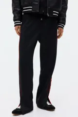 Pantalón jogger negro de corte relajado, con cordón ajustable en la cintura, franjas laterales rojas y estampado con la palabra "Honda" en la pierna izquierda.