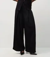 Pantalón de sastrería color negro, con cintura estructurada, pliegues delanteros, corte recto y cierre asimétrico.