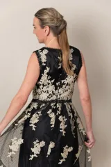Vestido largo de tul negro con bordado dorado de flores. Tiene escote en V cruzado, sin mangas y falda amplia.