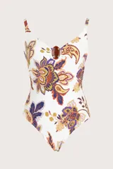 Malla enteriza con escote en V, tirantes finos y detalle de pieza decorativa en tono carey en el centro del pecho. Presenta un estampado botánico multicolor sobre fondo blanco.