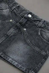 Minifalda de jean rígido color negro con efecto lavado acid wash, tiro bajo y diseño de bolsillos delanteros superpuestos con detalles de tachas metálicas.