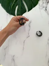 Aros tipo argolla trenzada en color negro con efecto de salpicaduras blancas, fabricados en arcilla polimérica.