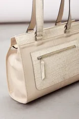 Cartera de cuero marrón de tamaño medio con diseño estructurado, que combina cuero liso y un panel frontal texturizado tipo cocodrilo con bolsillo exterior con cierre. Cuenta con doble asa de hombro y costuras visibles de contraste.