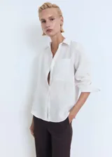 Camisa de lino blanca con cuello camisero, cierre frontal de botones, manga larga y bolsillo aplicado en el pecho.