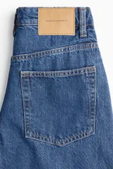 Jean de corte baggy con tiro alto, confeccionado en denim de algodón. Presenta diseño de cinco bolsillos, cierre frontal con botón y piernas con volumen en la zona de la cadera que se estrechan ligeramente hacia el bajo.
