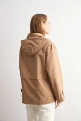 Trench color camel con capucha desmontable, cierre frontal con cremallera, bolsillos laterales y mangas largas con ajuste en puños.