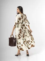 Vestido largo color crudo con estampado floral marrón, escote en V cruzado, mangas tres cuartos con volados y falda con niveles fruncidos.