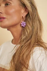 Aros colgantes dorados con diseño trenzado en la parte superior y un aplique de flor voluminosa en tono lila.