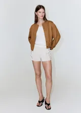 Chaqueta de diseño corto en tono tostado, confeccionada con mezcla de lyocell, algodón y lino. Presenta cuello redondo, mangas largas abullonadas, elásticos en los laterales y cierre frontal de botonadura visible.