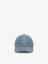 Gorra de denim azul con visera corta y logo metálico plateado en el frente.