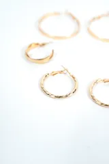 Set de tres pares de aros tipo argolla dorados, de diferentes tamaños y diseños: un par grande de aro fino liso, un par mediano de aro más ancho y liso, y un par pequeño con textura retorcida.