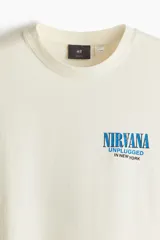 Remera de algodón color crema con cuello redondo acanalado y mangas cortas. Presenta un estampado pequeño en el pecho con el logo de Nirvana y la leyenda Unplugged in New York.