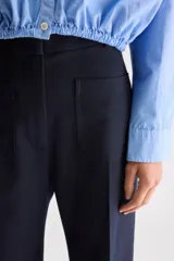 Pantalón azul marino de tiro alto y calce ajustado con diseño acampanado. Presenta bolsillos aplicados en el delantero y cierre frontal.