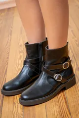 Bota corta de cuero charolado color bordó, con suela plana de goma negra, cierre lateral y tiras decorativas con hebillas metálicas en el tobillo.