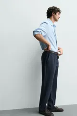 Pantalón de corte recto confeccionado en tejido elástico, con cintura elástica, pliegues frontales, bolsillos laterales y bolsillos traseros de vivo con botón.