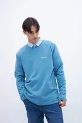 Buzo celeste de felpa liviana con cuello redondo, puños en mangas y bajo holgado. Tiene un bordado pequeño en el pecho con la inscripción "Uniform St.".