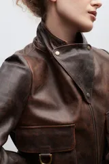 Blazer de cuero marrón con cierre frontal, cuello alto, múltiples bolsillos con hebillas y detalle de triángulo de cuero en el pecho.