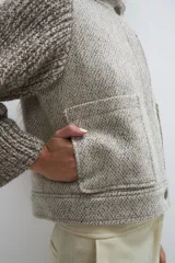 Campera de lana fina color crema, con cuerpo estructurado y mangas de tejido de punto acanalado. Presenta cuello alto, cierre frontal con botones y bolsillos laterales con doble abertura.