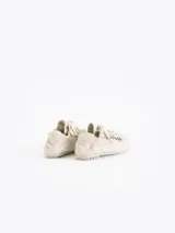 Zapatillas urbanas de cuero vacuno en color beige, con detalles de volados en los laterales de los cordones y suela de goma plana con textura.