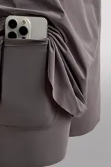 Short de running 2 en 1 color beige, confeccionado en tejido técnico ligero y elástico con malla interior integrada. Presenta cintura elástica ajustable con cordón, bolsillo trasero con cierre y aberturas laterales en el bajo.