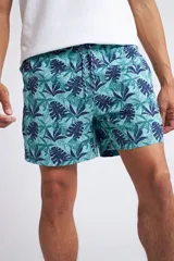 Short de baño con cintura elástica y cordón ajustable, confeccionado en tela ligera de secado rápido. Presenta un estampado botánico integral en tonos amarillos, blancos y azules, con dos bolsillos delanteros y uno posterior.
