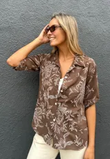 Camisa de corte recto y manga corta con cuello clásico y cierre frontal de botones. Presenta un estampado floral en color blanco sobre una base de color chocolate.