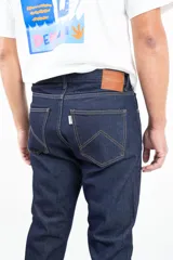 Jean clásico de corte recto, cinco bolsillos, color azul oscuro. Confeccionado en denim de 14 onzas sin elastano, con botones de cobre y costuras color camel.