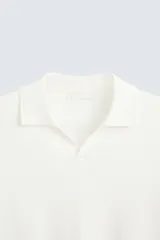 Jersey de punto color verde oliva, de calce relajado (relaxed fit), con cuello solapa y abertura frontal en forma de V. Es de manga corta y presenta acabados en rib en puños y ruedo.