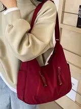 Bolso hobo grande color gris topo, de tela suave y liviana, con correa de hombro ajustable y dos bolsillos frontales con cierre.