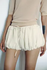Shorts de tiro bajo con diseño abullonado, confeccionado en tejido ligero con sutiles rayas verticales. Presenta cintura elástica ajustable con cordón y detalle de volantes en la parte superior.
