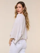 Blusa de algodón y rayón color beige, de la marca Dash. Presenta diseño texturado con sutiles rayas verticales, escote en V cruzado, mangas tres cuartos amplias y ruedo elastizado.