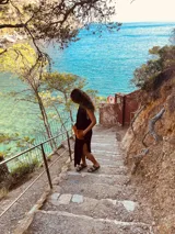 Vestido largo tejido de algodón color negro, sin mangas, con cuello redondo y tajos laterales. Presenta dos bolsillos de cuero color marrón en el frente.